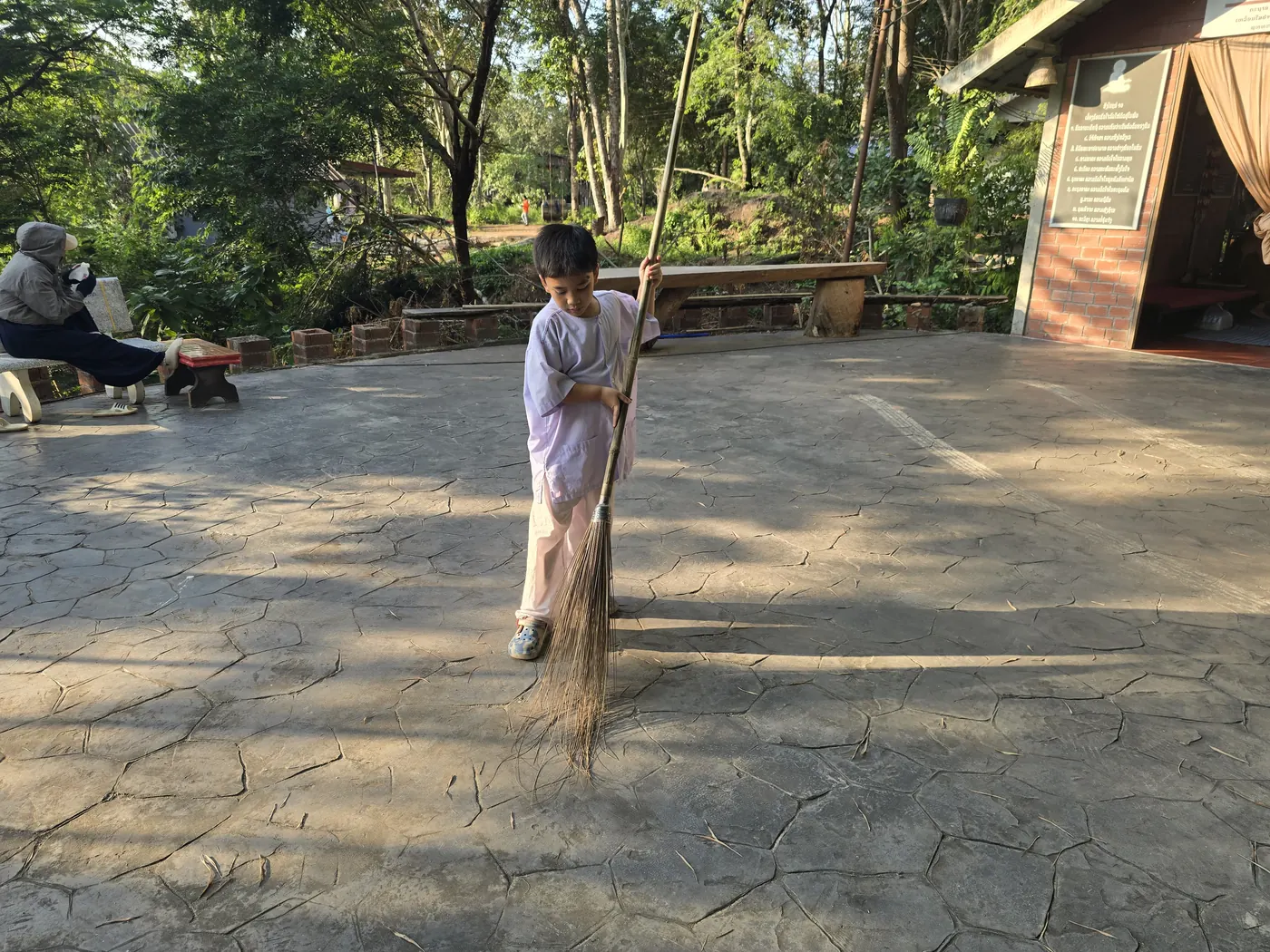 ເດັກນ້ອຍນຸ່ງຊຸດຂາວປັດກວາດລານວັດໃນຍາມເຊົ້າ